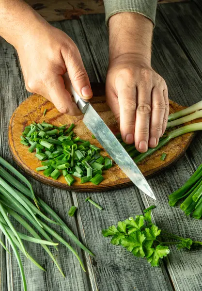 Elleri ustalıkla yeşil soğan ve otları, sıcak bir mutfakta, ahşap bir tahta üzerinde doğruyor. Güneş ışığı filtreler, taze malzemeleri ve eylemi vurgular..