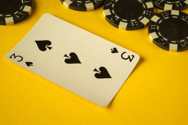 Siyah poker çipleriyle çevrili parlak sarı bir yüzeye maça üç kartı yerleştirilir. Sahne, arkadaşların kağıt oynamaları için davet edici bir atmosfer yakalıyor..