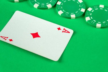 Poker fişleri parlak yeşil bir yüzey üzerinde bir karo ası etrafına saçılmış, bir kart oyunu için cazip bir atmosfer yaratıyor, hayranlar için ideal bir ortam ya da kumarhane seti..