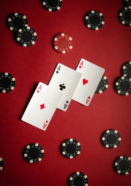 Siyah ve kırmızı poker çipleriyle çevrili kırmızı bir masada üç as sergileniyor. Bu da bir kumarhanede poker oyununda önemli bir an olduğunu gösteriyor..