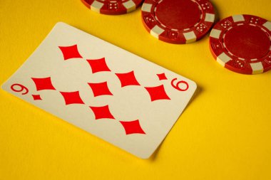 Karo dokuzlu bir kart parlak sarı bir yüzeye oturur, yanında da devam eden bir kart oyunu ya da poker oturumunu gösteren kırmızı poker fişleri vardır..