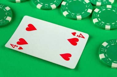 Kalbi olan tek bir kırmızı kart ve dört numara yeşil poker fişleri ile çevrili parlak yeşil bir yüzey üzerinde yatıyor..
