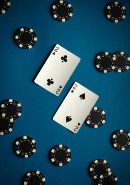 Sinek ikilisi ve maça ikilisi içeren iskambil kartları mavi bir masaya yerleştirilir. Çevrelerinde çok sayıda siyah poker fişi var. Oyun gecesi için heyecan verici bir ortam hazırlıyorlar..