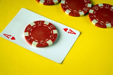 Yakın plan, Ace of Hearts kartının yanında parlak sarı bir yüzey üzerinde kırmızı bir poker çipi gösteriyor. Oyun oynamak ve sosyalleşmek için mükemmel bir atmosfer sunuyor..