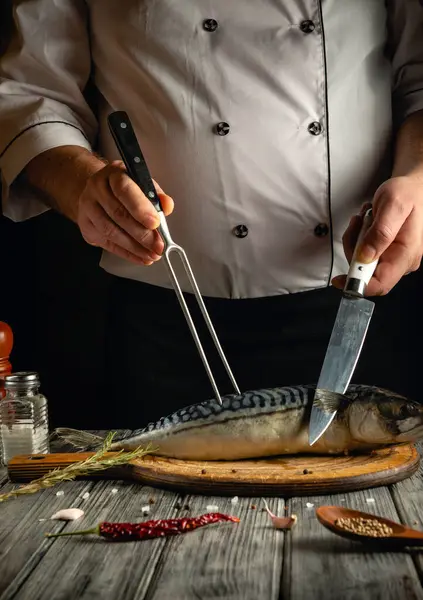 Bir şef, akşam sıcak bir mutfak ortamında bıçak ve çatal kullanarak ahşap bir kesme tahtasının üzerinde taze bir uskumru hazırlıyor..