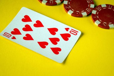Kupa onlu bir kart, kırmızı poker çiplerinin yanında parlak sarı bir yüzeye uzanır. Bu da sosyal bir etkinlik sırasında canlı bir kart oyunu olduğunu gösterir..