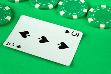 Maça kartlarından üçü çeşitli poker fişleri ile çevrili canlı yeşil bir keçeli yüzeye uzanır. Bu da gece yarısı poker oyununun heyecan verici olduğunu gösterir..