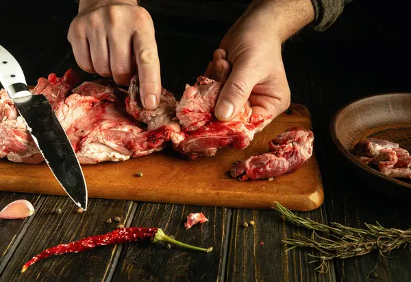 Elleri ustalıkla taze eti otlar ve baharatlarla çevrili ahşap bir kesme tahtasına ayırır. Sıcak ışık, canlı renkleri yükselterek, evcil bir atmosfer yaratır..