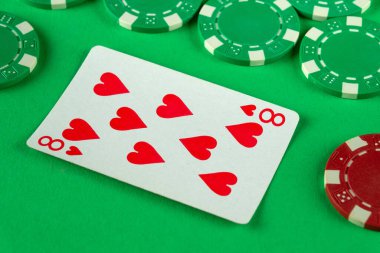 Canlı yeşil bir keçeli masa, birkaç poker çipinin yanında kupa sekizlisi sergiliyor. Oyuncular için heyecan verici bir kumarhane ortamı olduğunu gösteriyor..
