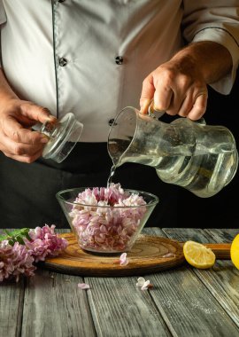 Şef, dilimlenmiş limon ve otlarla çevrili taze akasya çiçekleriyle dolu bir kaseye bir sürahi su döker. Mutfağın sıcak atmosferi kvass yapmak için mutfak becerilerini geliştirir..