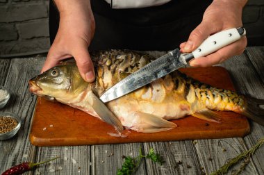 Filetleme işlemi sırasında ahşap bir tahtanın üzerindeki taze balığı ustalıkla tutan eller. Şef, kırsal mutfak atmosferinde ustaca teknikler gösteriyor..