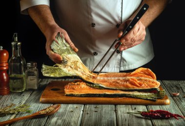 Bir şef büyük bir balık filetosunu kesme tahtasında ustalıkla idare eder. Yakınlarda çeşitli baharatlar ve otlar var. Mutfaktaki mutfak atmosferini arttırıyorlar..