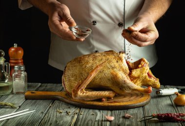 Bir şef, ahşap kesme tahtasına yerleştirilmiş bir tavuğun üzerine baharat serper. Modern bir mutfakta mutfak yetenekleri sergiler..