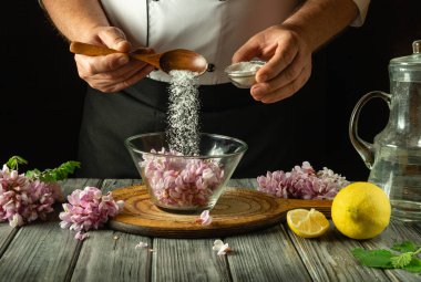 Bir şef ustalıkla bir kase taze çiçeğe şeker ekler ve ahşap tezgahta bir limon hazırlar. Samimi bir mutfakta, titiz mutfak sanatını sergiler. Akasya ile kvass yapmak.