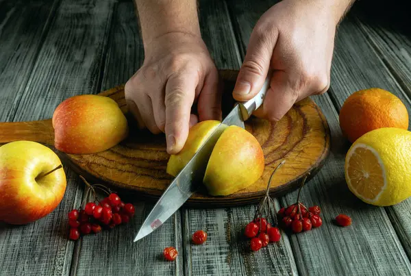 Elleri ustalıkla kesilmiş elmalar ve limonlar ahşap bir tahtanın üzerinde sıcak bir mutfakta taze meyvelerle çevrili. Odak noktası ürünün canlı renkleri ve dokuları..