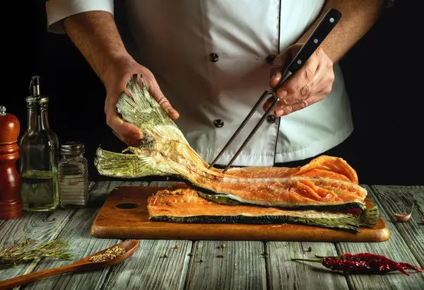 Bir şef büyük bir balık filetosunu kesme tahtasında ustalıkla idare eder. Yakınlarda çeşitli baharatlar ve otlar var. Mutfaktaki mutfak atmosferini arttırıyorlar..
