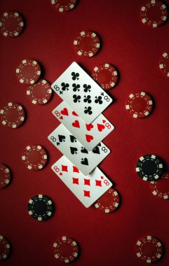 Koyu kırmızı bir yüzeye dizilmiş dört sekizli oyun kartları renkli poker çipleriyle çevrili bir oyun gecesi için canlı bir atmosfer yaratıyor..