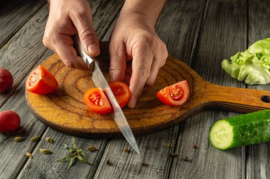 Taze domatesler ahşap bir kesim tahtasıyla dilimleniyor, yanında da salatalık ve marul var. Bu canlı mutfak sahnesi sağlıklı yemekler hazırlamanın sevincini gözler önüne seriyor..