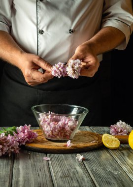 Bir şef sofistike bir içecek hazırlamak için çiçek yapraklarını dikkatlice kaldırır. Taze limon dilimleri ve otlar mutfaktaki sıcak atmosferde cam bir kasenin etrafını sarar..