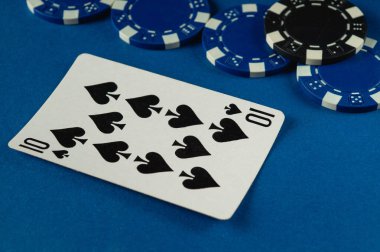 Çeşitli renkli poker çipleriyle çevrili mavi bir yüzey üzerinde duran maça onlu bir oyun kartının yakın plan çekimi, bir kart oyunu için enerjik bir atmosfer yaratıyor.