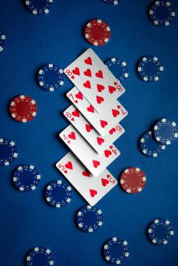 İskambil kâğıtları düz floş kalpler düzgün istiflenmiş kırmızı ve mavi poker fişleri etrafa saçılmış oyun gecesi için canlı bir atmosfer oluşturur.