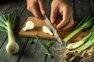 Kesme tahtasındaki taze soğanları ustalıkla dilimle. Köy mutfağı ahşap yüzey ve doğal ışık ile güçlendirilerek canlı sebzeleri ön plana çıkarıyor..