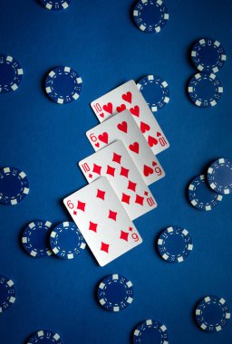 Kalpleri ve elmasları gösteren iskambil kağıtları koyu mavi bir yüzey üzerinde bir fan şeklinde uzanır. Mavi poker fişleri etrafa saçılmış durumda. Bu da devam eden bir oyun olduğunu gösteriyor..