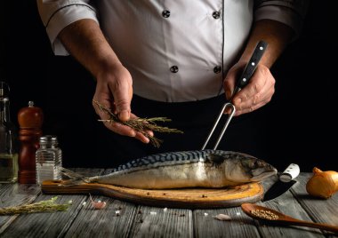 Bir şef ustalıkla ahşap bir kesme tahtasının üzerinde taze bir uskumru hazırlar, mutfak aletleriyle çevrili iken şifalı otlar ekler. Karanlık, rahat bir atmosfer mutfak odağı arttırır..