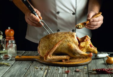 Bir şef, kaşık kullanırken baharatlarla pişirilmiş ördeği ustalıkla pişirir. Mutfak düzeninde çeşitli yemek malzemeleri ve çatal bıçaklar yer alıyor..