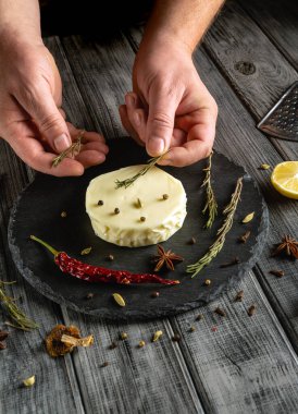 Eller, baharatlar ve limon dilimleriyle çevrili dairesel bir peynire taze otları nazikçe yerleştirir ve bir aşçılık atölyesinde lezzet sanatını sergiler..