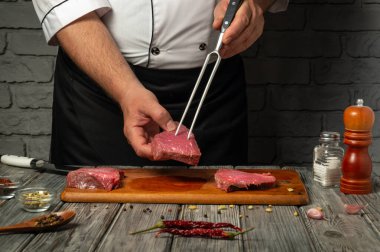 Bir şef, çiğ eti çatalla ustalıkla idare ediyor. Etrafı baharat ve malzemelerle dolu. Geceleri kırsal bir mutfak ortamında ahşap bir tahtanın üzerinde..