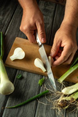Eller ahşap kesme tahtasındaki taze soğanları ustalıkla kesiyor. Mutfak canlı ürünler ve topraksı dokularla dolu. Yemek pişirme atmosferini arttırıyor..