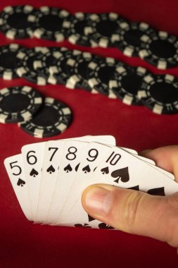 Bir el, beş, altı, yedi, sekiz ve on maça poker kartını gösterir. Siyah çipler canlı kırmızı bir keçeli masaya istiflenmiş. Bu da heyecanlı bir oyunu işaret ediyor..