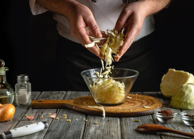 Şefin elleri ahşap bir masada şeffaf bir kâseye lahana öğüterek yağ, sarımsak ve baharat gibi malzemelerle çevrelenmiş lezzetli bir yemek yaratıyor..