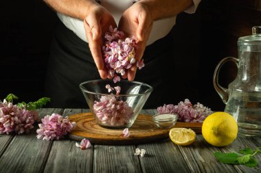 Şef akasya çiçekleri ve limondan lezzetli ve sağlıklı bir kvass hazırlıyor. İçecekler mutfak masasının üzerine konur..
