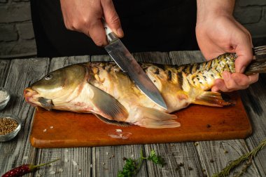 Bir aşçı ustaca fileto yapıyor. Sıcak bir mutfakta, ahşap bir kesme tahtasının üzerinde bütün bir balığı. Taze bitkiler ve baharatlar yakınlarda düzenlenir, mutfak atmosferini güçlendirir..