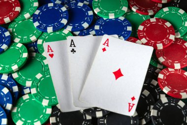 Üç iskambil kartı çeşitli renklerde poker çiplerinin üzerinde asların dinlendiğini gösteriyor. Heyecan verici bir kart oyunu akşamında cazip bir atmosfer yaratıyor..
