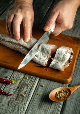 Eller ahşap bir yüzeyde taze bir balığı dilimliyor. Yakınlarda, kurutulmuş biber ve bir kaşık kişniş tohumu sıcak bir mutfakta kırsal bir yemek atmosferi yaratır..