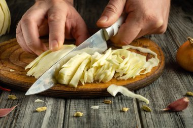 Keskin bıçak gevrek lahanayı keser, tahta tahtada ince dilimler oluşturur. Eller ustalıkla bıçağı manevra ettirir. Soğanlar yakınlarda otururken taze ürünler sağlıklı pişirme sinyalleri veriyor..