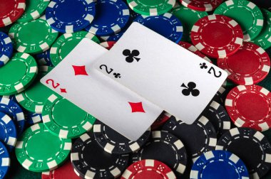 Renkli poker fişleri iki numarayı gösteren iki iskambil kağıdının etrafına saçılmış. Bu da arkadaşlar arasında çekişmeli ve rekabetçi bir kart oyunu oynandığını gösteriyor..
