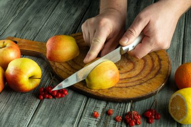 Eller ustalıkla rengarenk meyvelerin arasında, rengarenk ahşap bir tahtanın üzerinde taze bir elma keserek mutfak ortamında davetkar bir atmosfer yaratıyor..