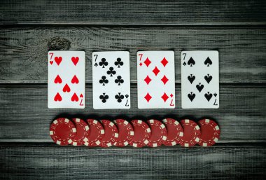 Kazanan dört yediliyi gösteren dört iskambil kağıdı, düzgünce istiflenmiş poker çiplerinin yakınındaki kırsal ahşap bir masanın üzerine serilmiş, heyecan verici bir oyun atmosferi yaratıyor..