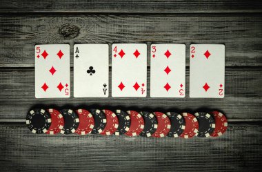 Elmas ve sinek ası içeren bir iskambil kağıdı kırsal bir ahşap masadaki bir sıra poker çipinin üzerinde oturup, kumar oynamak için havayı hazırlıyor..