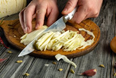 Eller ahşap bir tahtanın üzerinde taze lahana doğruyor ve sağlıklı malzemelerin hazırlanmasını vurguluyor. Mutfağın kırsal cazibesi yemek hazırlama sürecine sıcaklık katıyor..