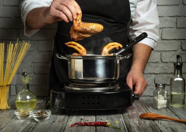 Bir şef fırında tavuk kanadı hazırlar. Etrafı baharat ve yağ gibi taze malzemelerle çevrilidir. Mutfakta tuğla arka planda kırsal bir titreşim var..