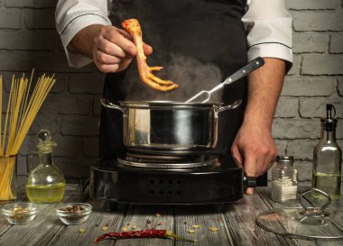 Bir şef, tavuğu ocağın üstündeki buharlı tencerenin üstünde tutmaya odaklanır. Mutfak atmosferini geliştirmek için tezgahın üzerine çeşitli yemek malzemeleri yerleştirildi..