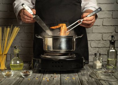 Bir şef fırında tavuk pişirirken maşa ve bıçak ustalıkla manevra yapar. Taze malzemeler ve baharatlar yakınlarda, davetkar bir yemek atmosferi yaratıyor..