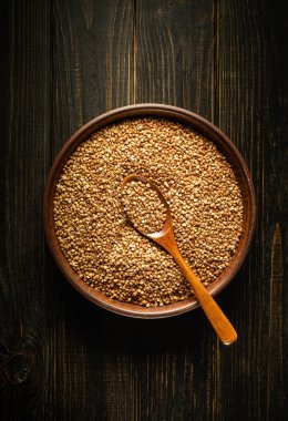 İçi kişniş tohumlarıyla dolu kase, koyu ahşap bir masanın üstünde duruyor. Tahta kaşık tohumların arasında duruyor, pişirmeye ya da baharata hazır..