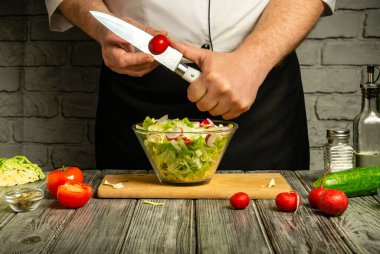Bir şef canlı bir salata hazırlarken kiraz domateslerini ustalıkla dilimler. Taze malzemeler ahşap bir yüzeye yerleştiriliyor ve kırsal bir mutfak atmosferi yaratıyor..