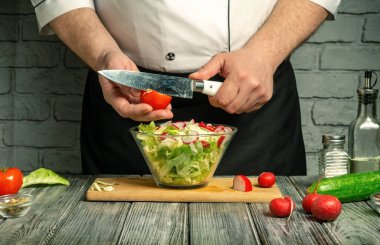 Bir şef sıcak bir mutfakta renkli bir salata hazırlarken domates ve turpları ustaca doğruyor. Taze sebzeler karıştırılmaya hazır cam bir kasenin etrafına dizilir..